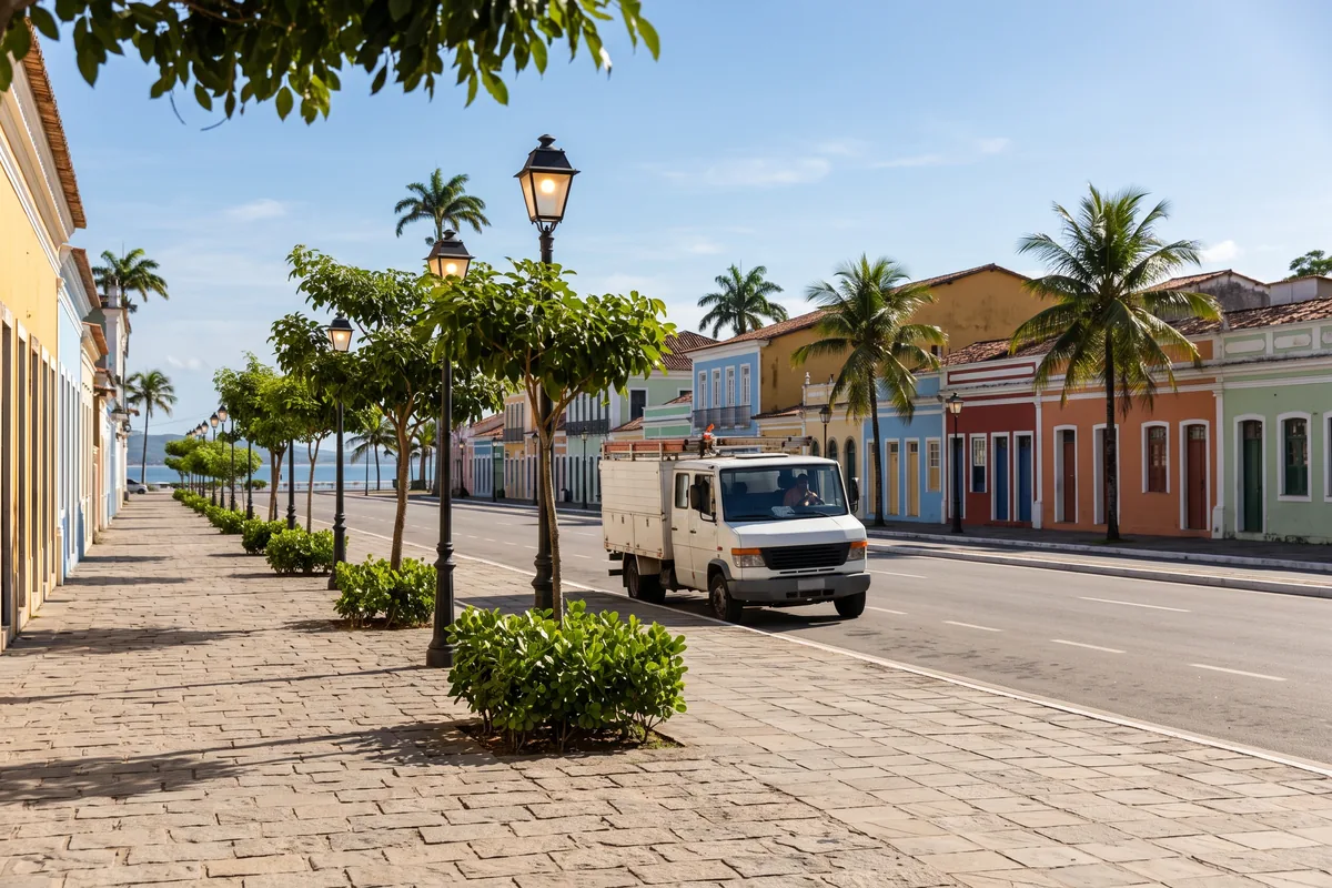 Avenida à beira-mar em Camaçari: calçada varrida, árvores podadas, luminárias em funcionamento e um caminhão de serviços da Prefeitura passando pela via.